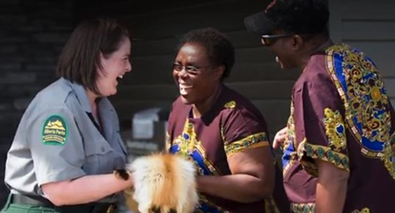 An Alberta Parks staff member holding a fur. She is showing the fur to two guests. All of the participants are laughing.