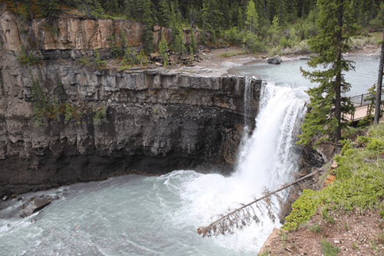A photo of Crescent Falls. A cloudy blue river falls over a steep cliff face into a wider portion of the river.