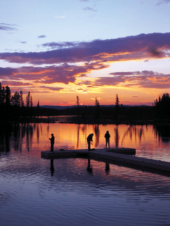 A sunset over Pierre Grey's Lakes Provincial Park. There are three silhouettes fishing on a dock. The sky is reflecting off the water.