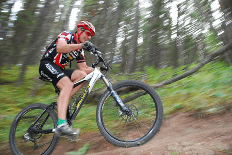 A biker in full gear biking through a forest. The background is blurred, implying the biker is going fast.