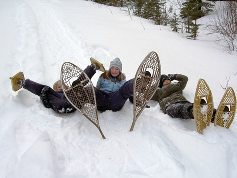 Three children in snowshoes fallen over, posing and laughing.